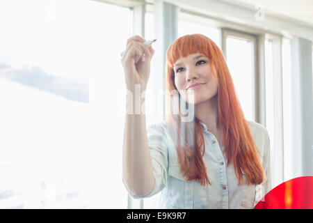 Creative businesswoman writing on glass wall in office Stock Photo