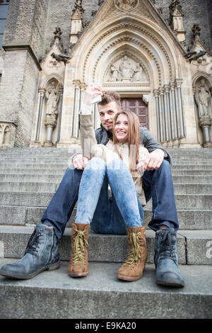 Full length of young couple taking selfie while sitting on steps outdoors Stock Photo