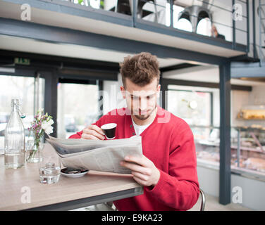 Young man reading newspaper while drinking coffee in cafe Stock Photo