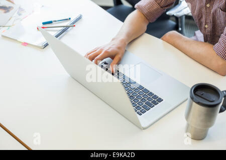 Cropped image of man using laptop at desk in creative office