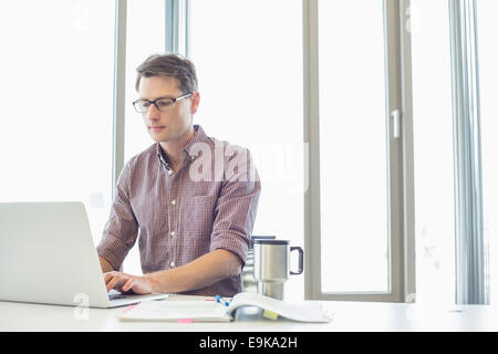 Businessman working on laptop at desk in creative office Stock Photo
