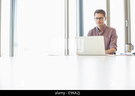 Thoughtful businessman looking away while using laptop at desk in creative office Stock Photo
