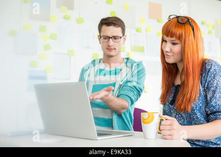 Businessman showing something to female colleague on laptop in creative office Stock Photo