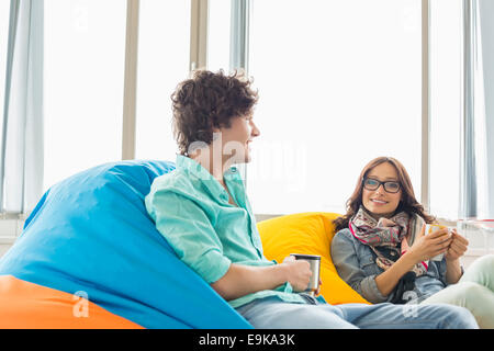 Business colleagues having coffee while relaxing on beanbag chairs in creative office Stock Photo