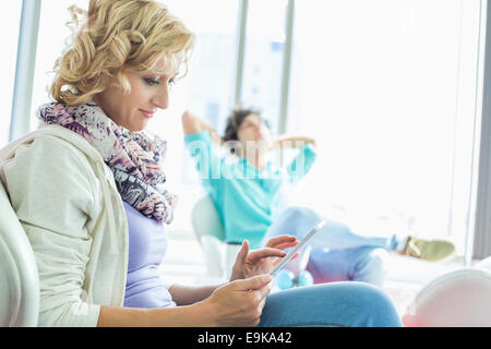 Creative businesswoman using digital tablet at lobby with colleague relaxing in background Stock Photo