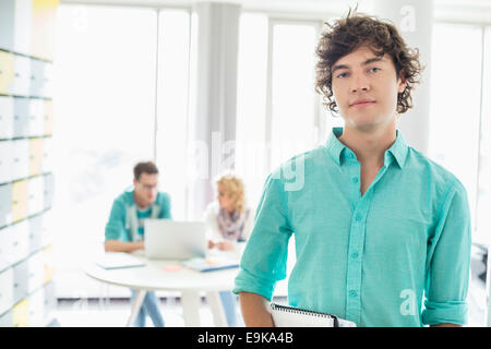 Portrait of confident businessman with colleagues working in background at creative office Stock Photo
