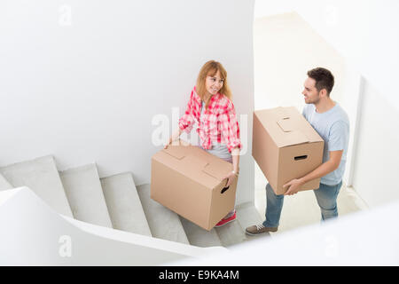 Happy couple carrying moving boxes up stairs in new house