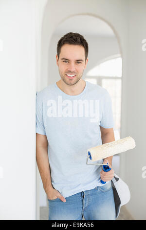 Portrait of handsome man holding paint roller in new house Stock Photo