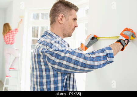 Man measuring wall with woman painting in background Stock Photo
