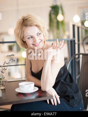 Happy young woman waving at restaurant table Stock Photo