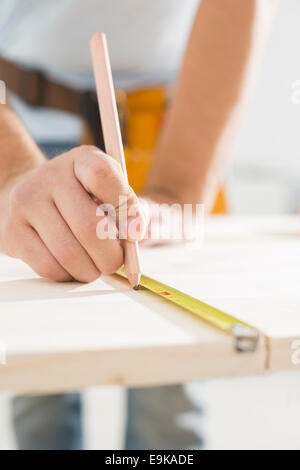 Midsection of carpenter marking table with measure tape Stock Photo
