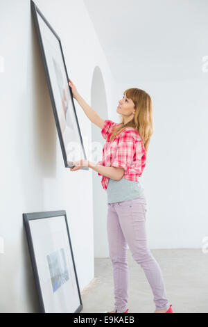 Woman hanging picture frame on wall in new house Stock Photo