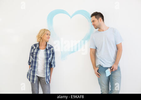 Mid-adult couple looking at each other with painted heart on wall Stock Photo