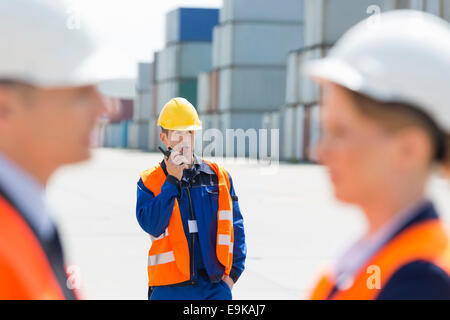 Worker using walkie-talkie while colleagues discussing in foreground at shipping yard Stock Photo