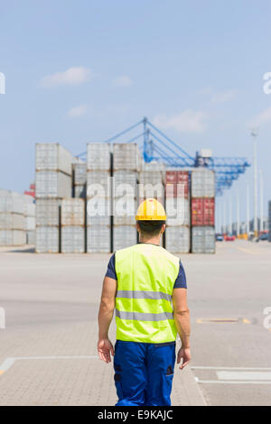 Rear view of mid adult worker walking in shipping yard Stock Photo