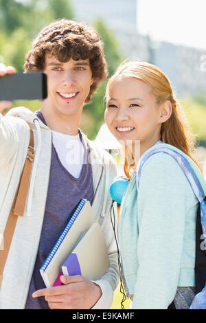 Male and female friends taking selfie with smart phone at college campus Stock Photo