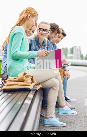 University students studying while sitting on low wall in park Stock Photo