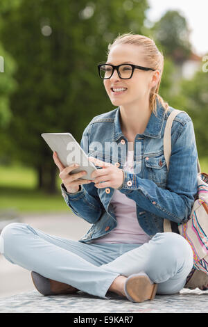 Full length of smiling young female college student using tablet PC in park Stock Photo