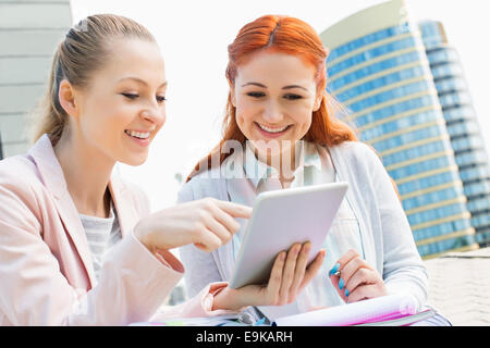 Smiling young university students using digital tablet against building Stock Photo