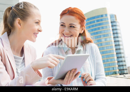 Smiling young university students using tablet PC against building Stock Photo