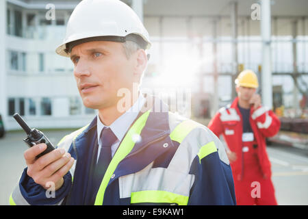 Male worker using walkie-talkie with colleague in background at shipping yard Stock Photo