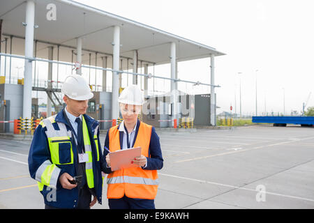 Male and female workers discussing over clipboard in shipping yard Stock Photo