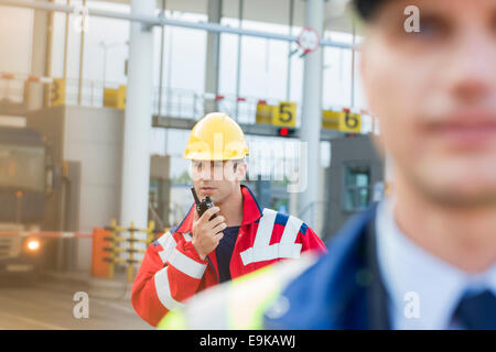 Male worker using walkie-talkie with colleague in foreground at shipyard Stock Photo