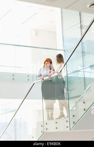 Businesswomen having coffee while standing on steps in office Stock Photo