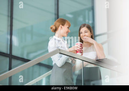 Businesswomen gossiping while having coffee on steps in office Stock Photo