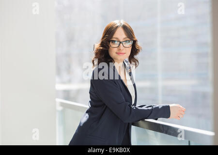 Portrait of confident young businesswoman leaning on railing in office Stock Photo