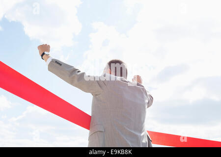 Rear view of businessman crossing finish line against sky Stock Photo