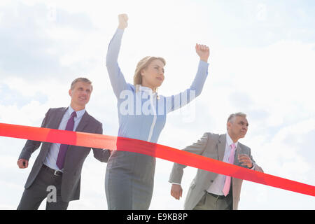 Businesswoman crossing finishing line with colleagues in background Stock Photo