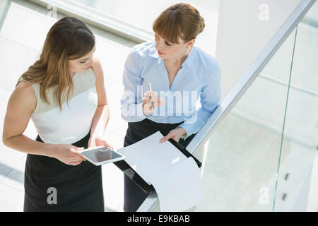 High angle view of businesswomen discussing over tablet PC and documents by railing in office Stock Photo