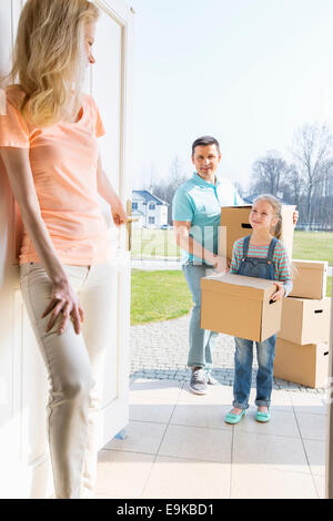 Woman looking at family with cardboard boxes entering new home
