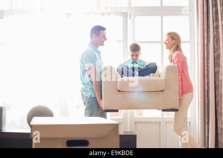 Happy parents carrying son on armchair in new house Stock Photo