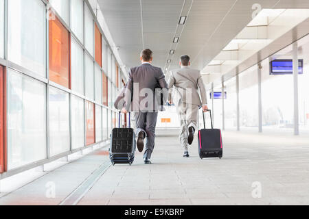 Full length rear view of businessmen with luggage running on railroad platform Stock Photo