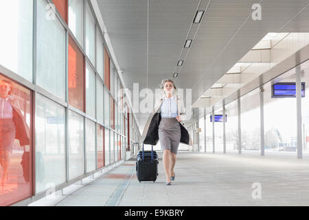 Full length of young businesswoman with luggage rushing in railroad station Stock Photo