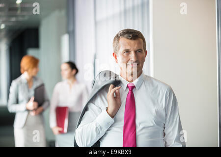 Businessman holding coat over shoulder with female colleagues in background at office Stock Photo