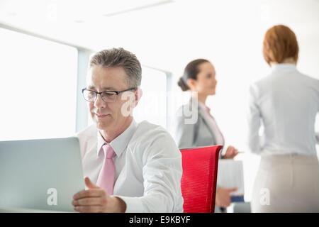 Businessman using laptop with colleagues discussing in background at office Stock Photo