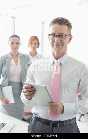 Portrait of happy businessman holding digital tablet with female colleagues in background at office Stock Photo