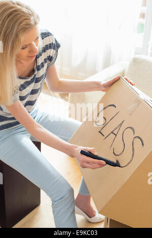 Woman labeling moving box with glass material at home Stock Photo