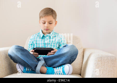 Boy playing hand-held video game on sofa Stock Photo