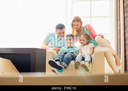 Family looking at boy playing hand-held video game at home Stock Photo