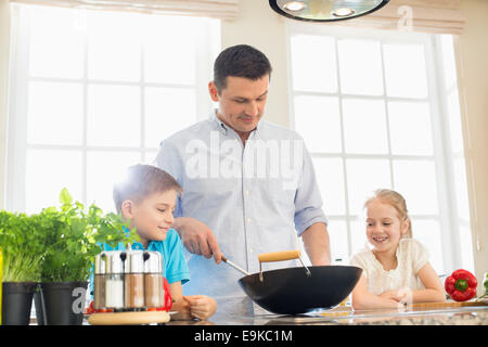 Children looking at father preparing food in kitchen Stock Photo