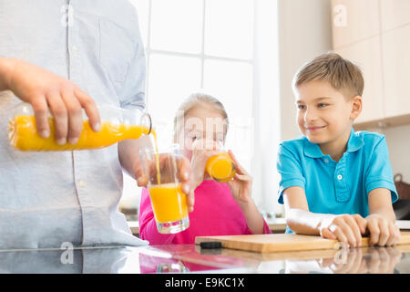 Midsection of father serving orange juice for children in kitchen Stock Photo