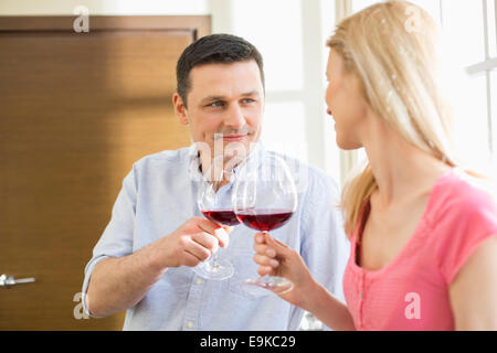 Couple toasting red wine glasses in kitchen Stock Photo
