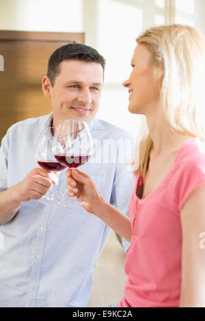Happy couple toasting red wine glasses in kitchen Stock Photo