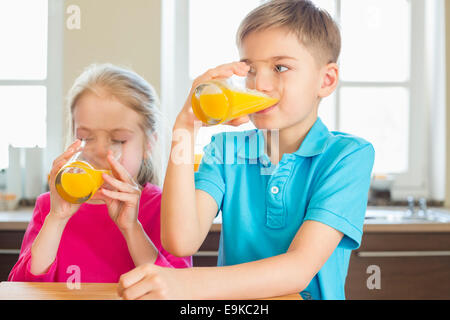 Siblings drinking orange juice in kitchen at home Stock Photo