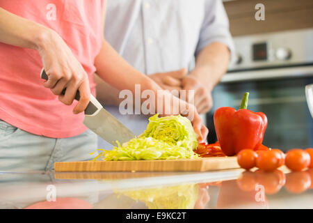 Midsection of woman chopping vegetables in kitchen with man standing in background Stock Photo
