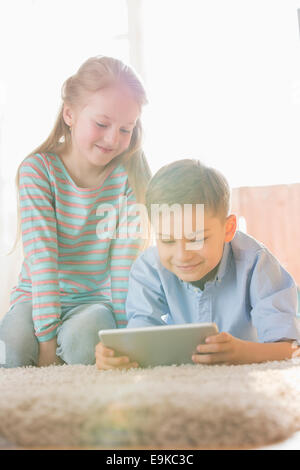 Siblings using digital tablet on floor at home Stock Photo